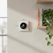 Thermostat rond mural blanc installé près d’une étagère décorative.